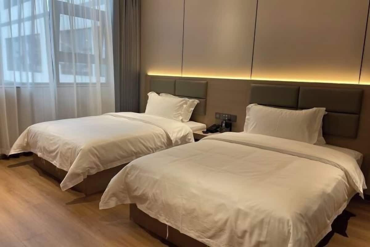 Habitación de hotel con dos camas, una mesita de noche y un cabecero moderno con iluminación integrada.