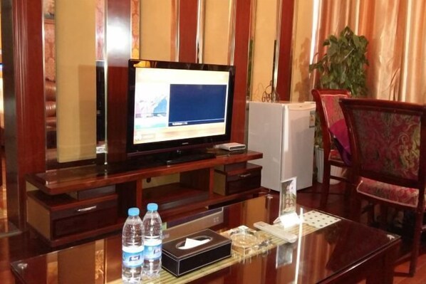 A hotel room with a wooden entertainment unit, a flat-screen TV, a small white appliance, a water bottle, a tissue box, and a decorative item on the table.