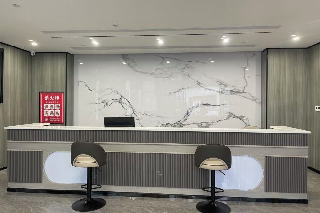 A reception desk with a marble back wall, two bar stools, and a red informational sign.