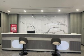 Un mostrador de recepción con un muro de mármol en la parte trasera, dos taburetes de bar y un letrero informativo rojo.