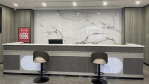 Een receptiebalie met een marmeren achterwand, twee barkrukken en een rood brandveiligheidsteken.