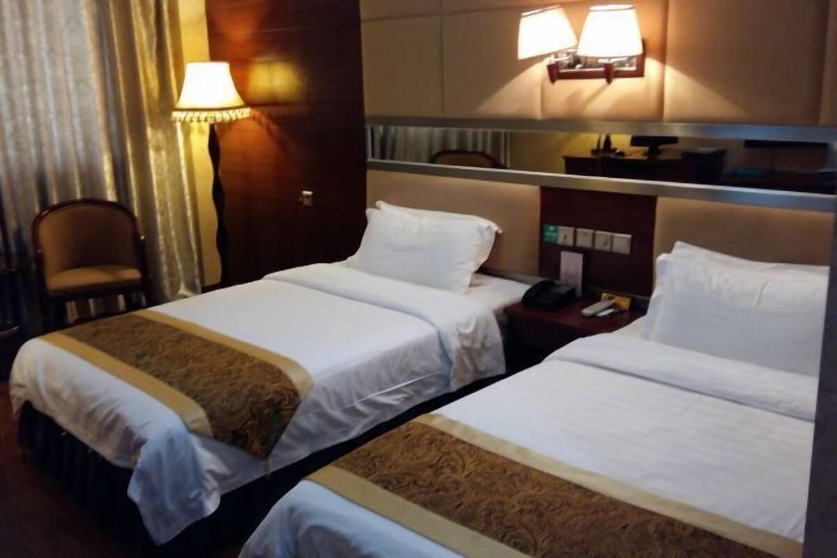 Una habitación de hotel con dos camas, una silla, una mesita de noche con lámpara y un espejo.