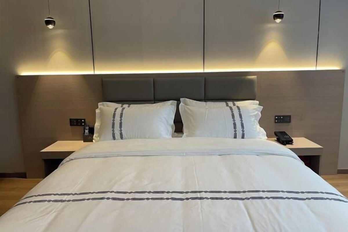A modern hotel room with a large bed, two bedside tables, and a headboard with integrated lighting.
