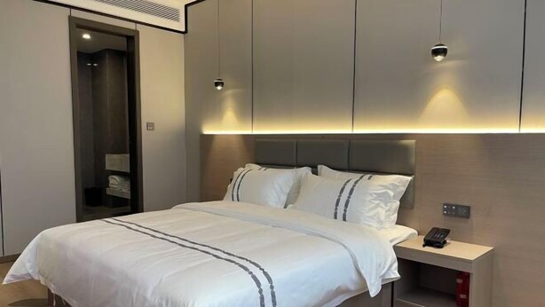 Een moderne hotelkamer met een groot bed, een nachtkastje met een telefoon, en inbouwmeubels.