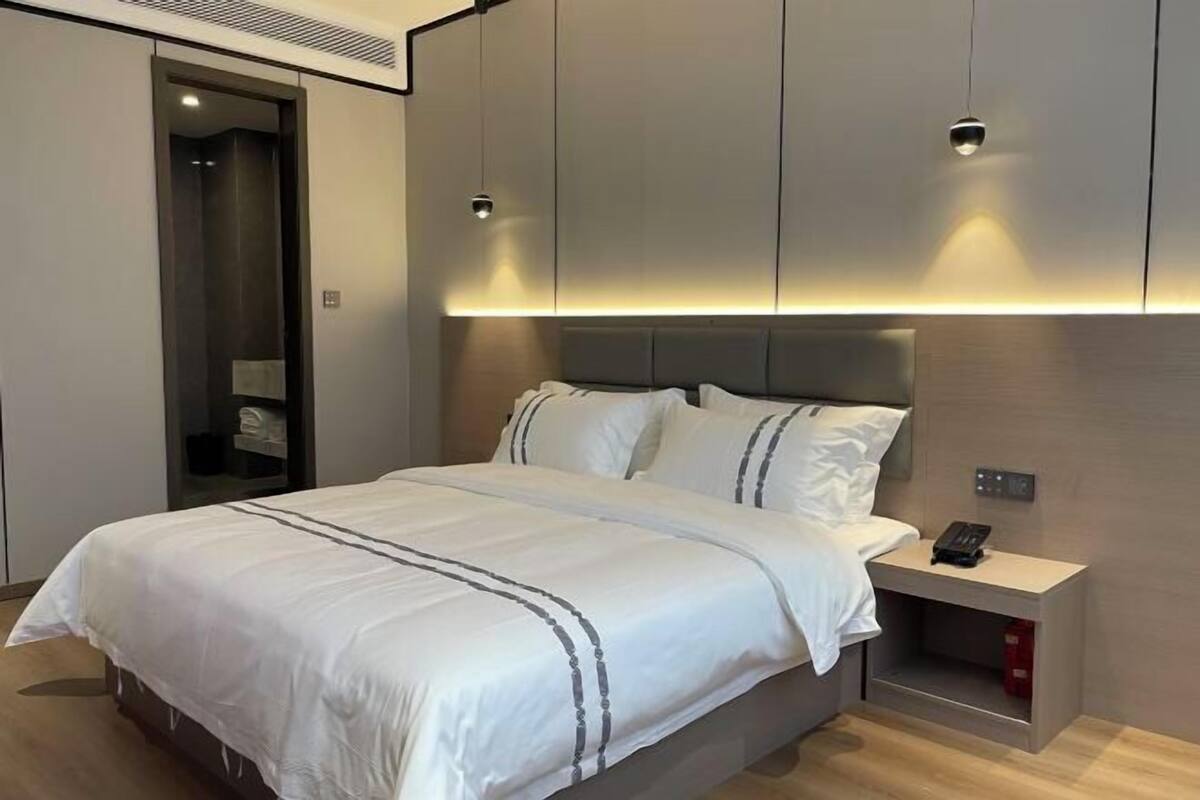 Una habitación de hotel moderna con una cama grande, una mesita de noche con teléfono y armarios empotrados.