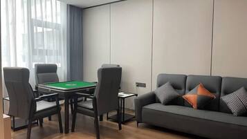 Uma sala de estar moderna com mesa de bilhar, um sofá com almofadas estampadas e uma grande janela com cortinas leves.