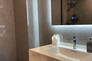 A modern bathroom with a large mirror, a white sink, and a towel dispenser.