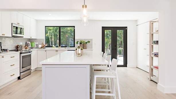 Una cocina moderna con armarios blancos, una isla central y un amplio ventanal con vista a zonas verdes.