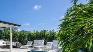 Una piscina con sillas de descanso blancas y una zona de estar cubierta.