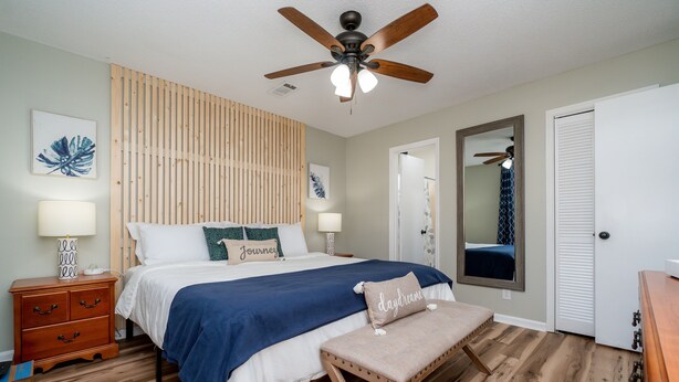 A bedroom with a bed, bedside tables, a bench, a ceiling fan, and a mirror. - AMAZING for Large Groups or Crews- 7 beds/ 4 bedrooms (Warner Robins)