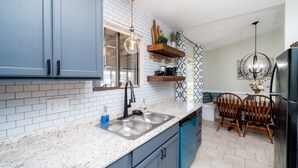 A kitchen with blue cabinets, a white tiled backsplash, a built-in dishwasher, and a dining area with a wooden table and chairs. - AMAZING for Large Groups or Crews- 7 beds/ 4 bedrooms (Warner Robins)