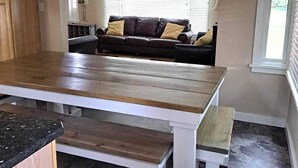 A kitchen with a wooden table and bench, a ceiling fan, and a sofa with cushions in the background. - Cowley Cozy Cottage 3 Bed/ 2 Bath (Cowley)