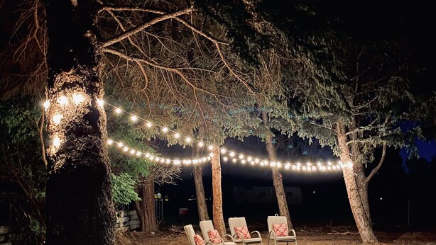 An outdoor seating area with chairs under a tree, string lights, and a dirt ground. - Cowley Cozy Cottage 3 Bed/ 2 Bath (Cowley)
