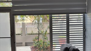 Un fauteuil relaxant doté d’un coussin et d’un oreiller, placé près d’une porte-fenêtre coulissante donnant sur une plante en pot et un bâtiment à l’extérieur.