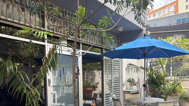 Un espace patio aménagé avec des sièges d’extérieur, des plantes en pot et un parasol bleu.
