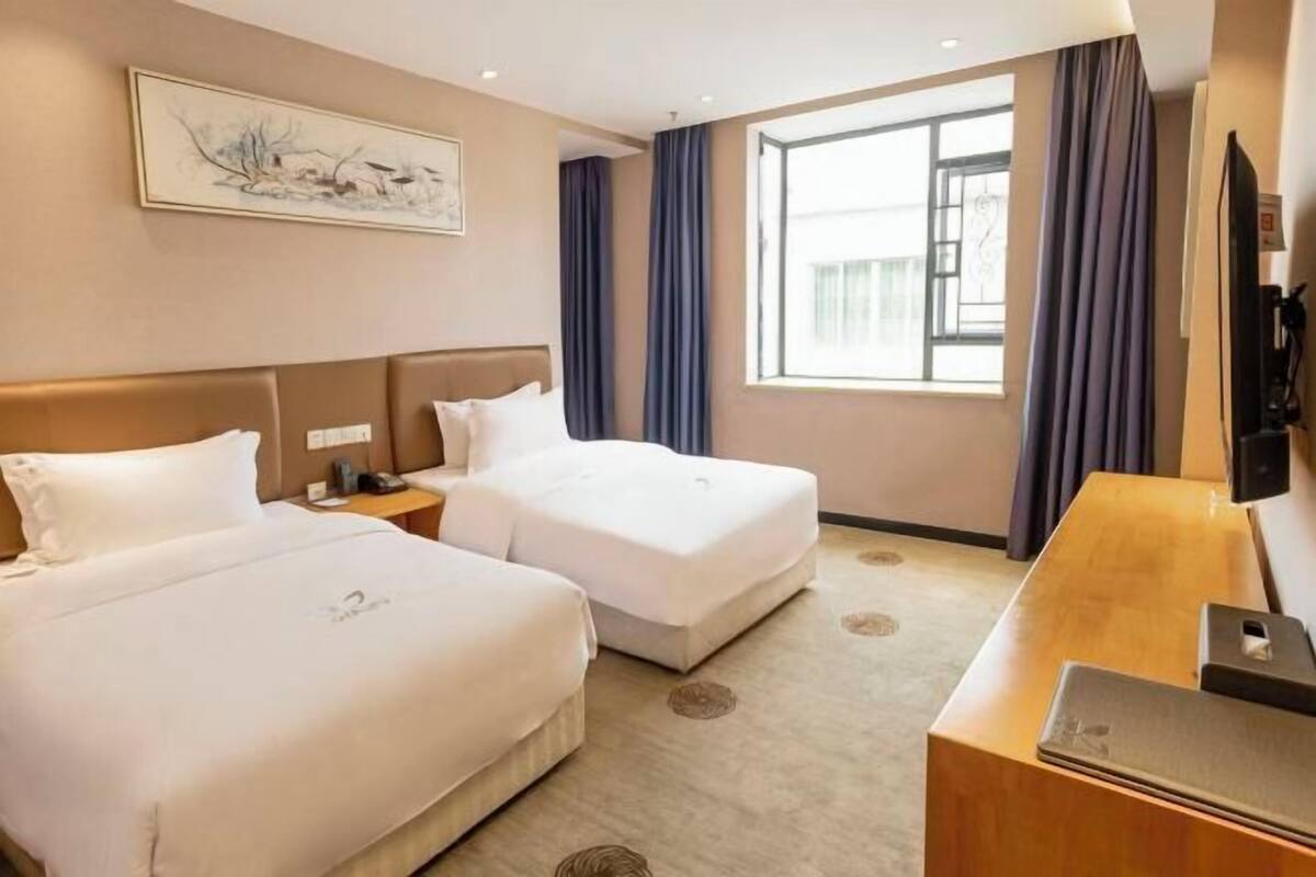 A hotel room with two beds, a desk, a TV, and a large window with curtains.