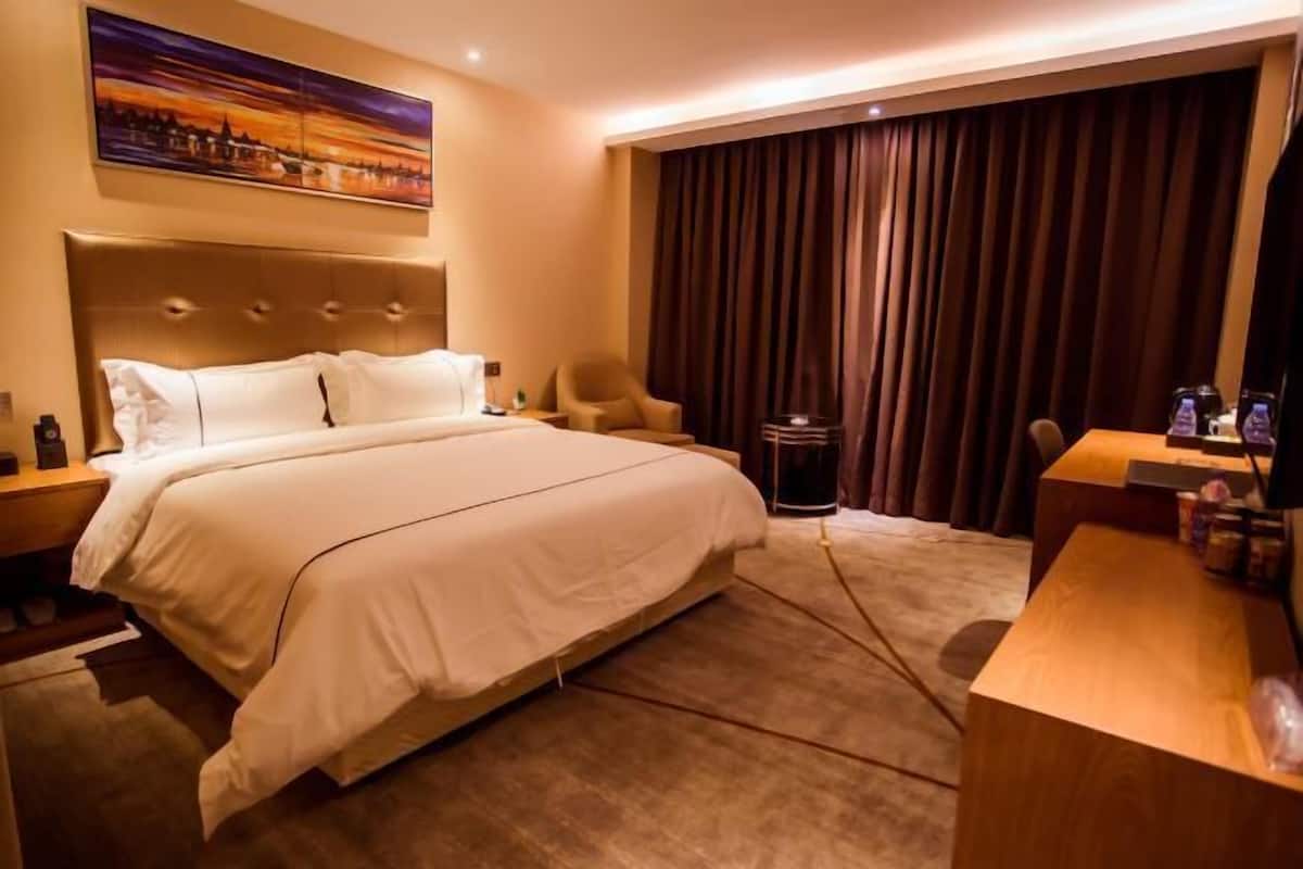 A hotel room with a large bed, a desk, a chair, a TV, and a painting on the wall.
