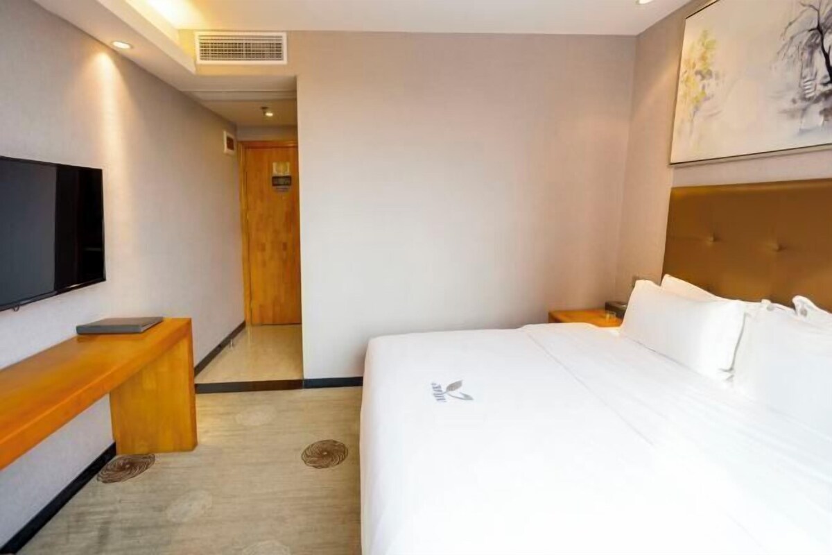 Habitación de hotel con cama, televisión, banco de madera y puerta que da a otra habitación.