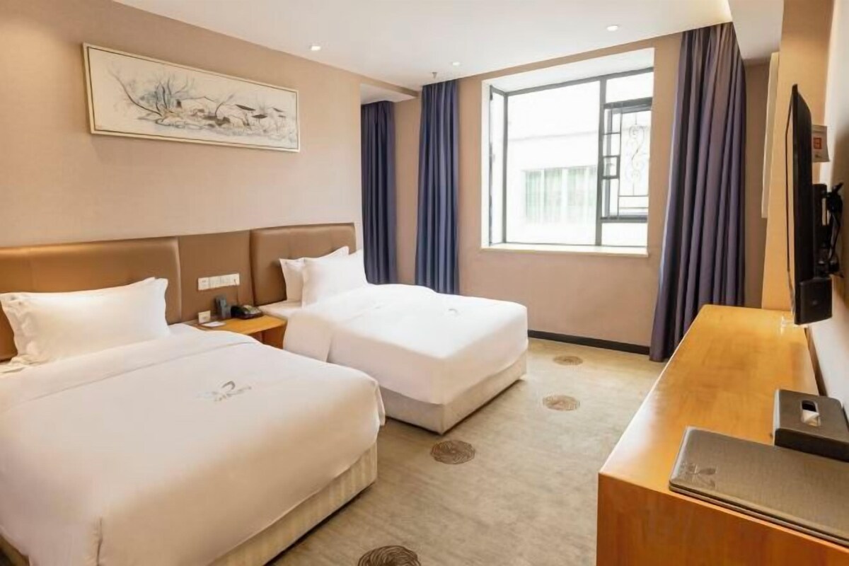 A hotel room with two beds, a desk with a laptop, a TV, and a window with curtains.