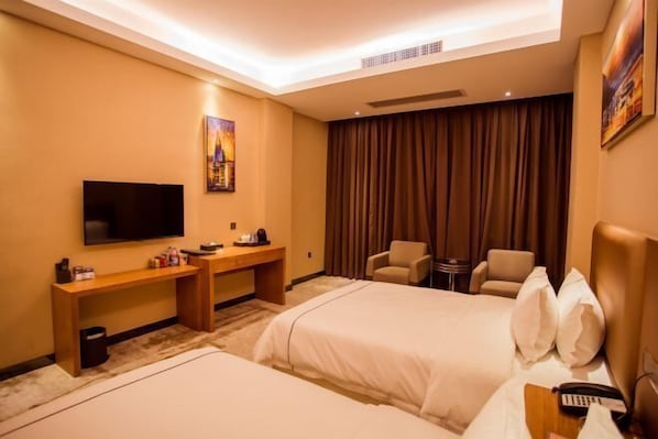 Habitación de hotel con dos camas, un escritorio, un televisor y una zona de estar con sillas.