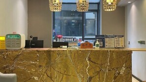 Una mesa de recepción con cubierta de mármol, un teléfono digital, una caja registradora y un pequeño letrero con forma de casa.