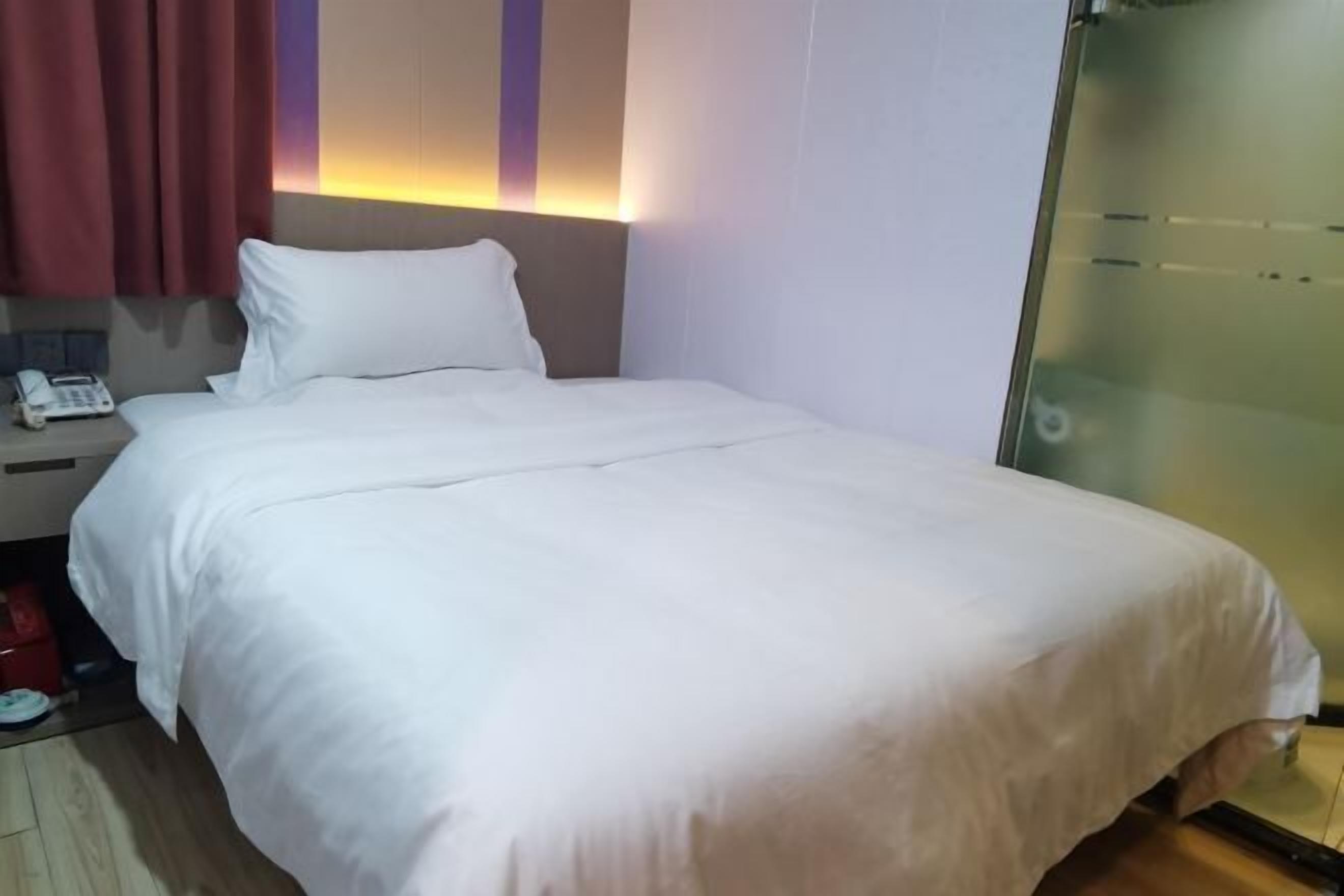 A hotel room with a bed, a nightstand with a phone, and a glass door.