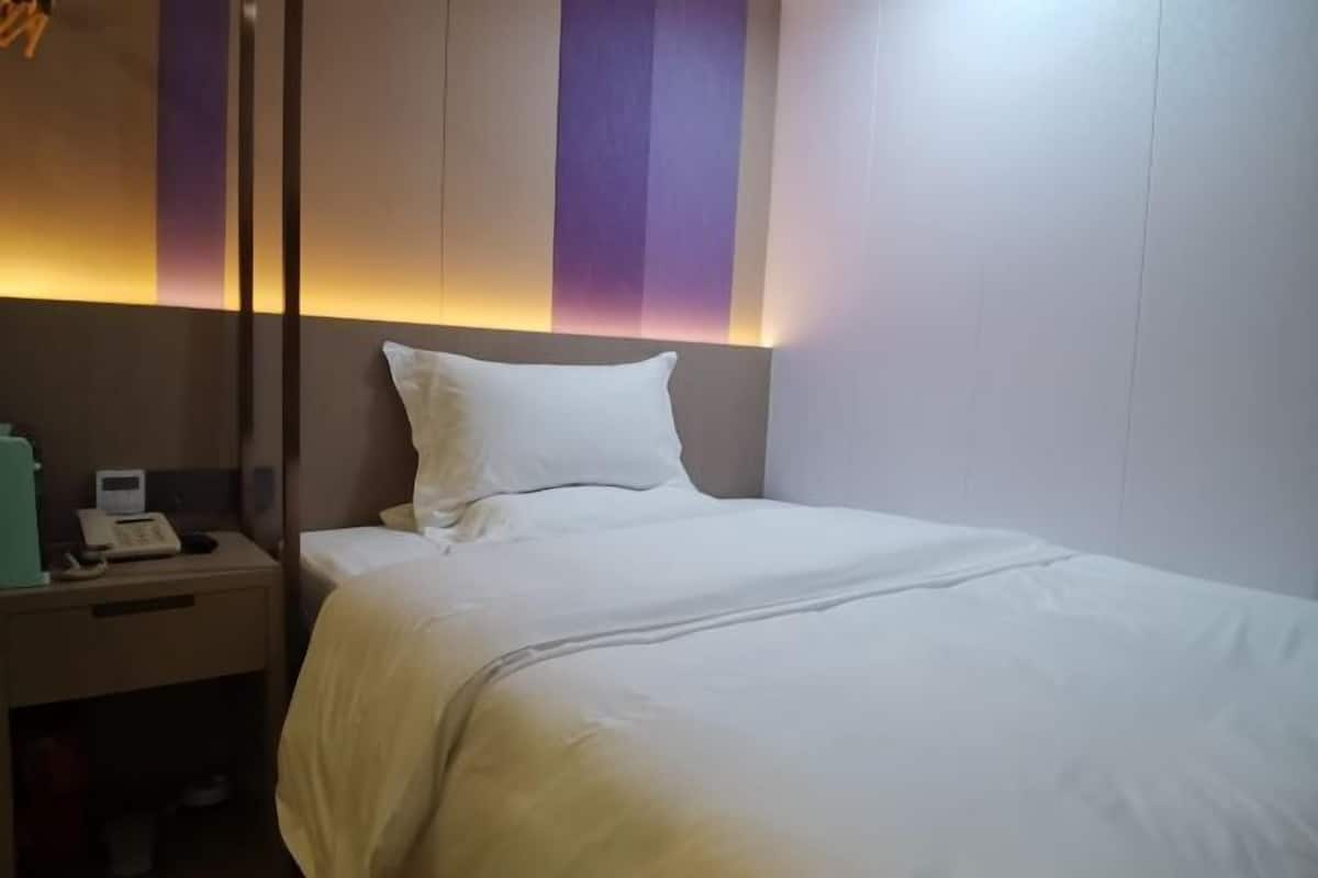A hotel room with a bed, a nightstand with a phone and a small table, and a wall with vertical stripes.