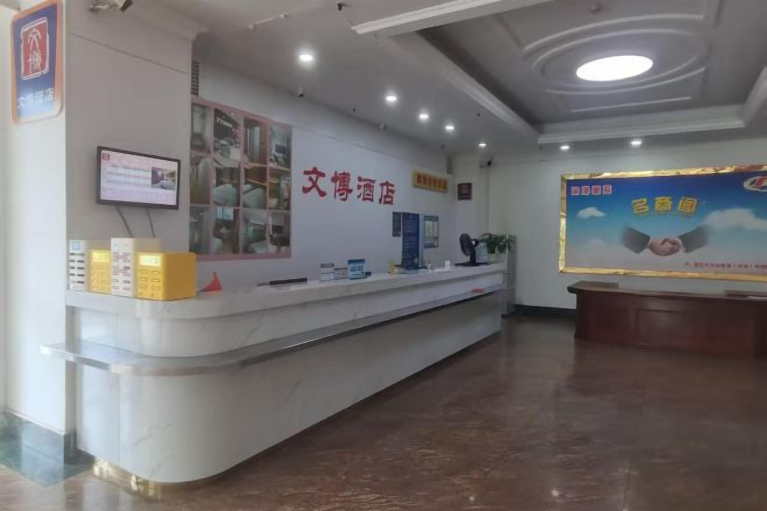 Zona de recepción de hotel con mostrador de mármol, pantalla digital y un cartel con texto.