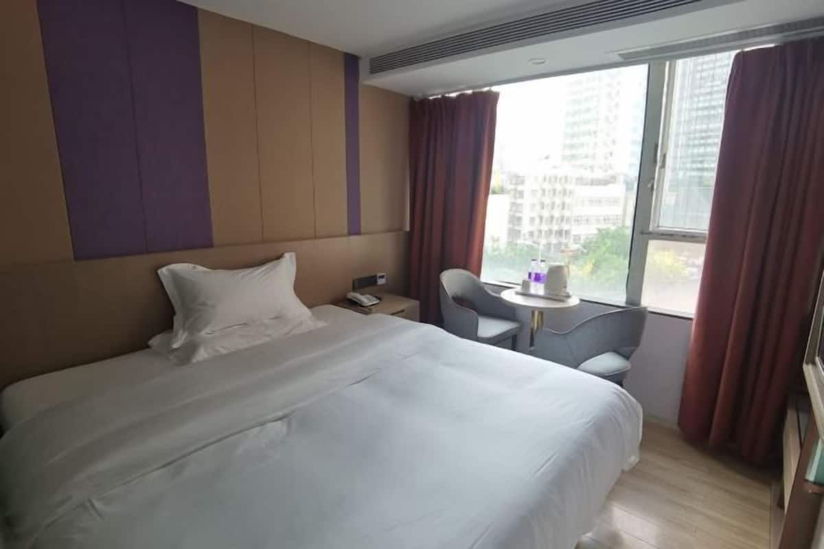 A hotel room with a bed, a desk, and a window with curtains.