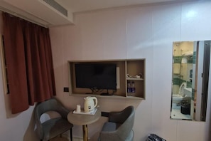 A small room with a TV, a table with a kettle and cups, two chairs, and a mirror reflecting a bathroom. - Wenbo Hotel (Shenzhen Diwang Building Hongling Subway Station) (Shenzhen)