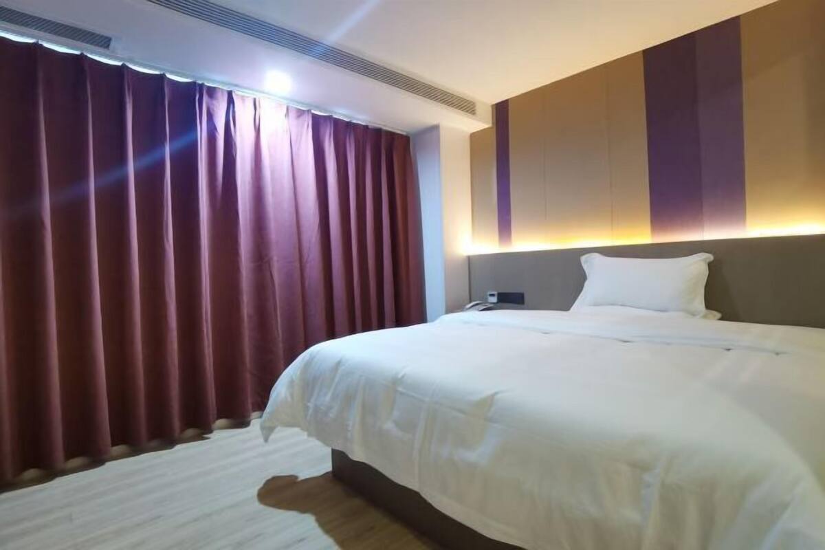 A hotel room with a bed, curtains, a wall-mounted light, and a rug.