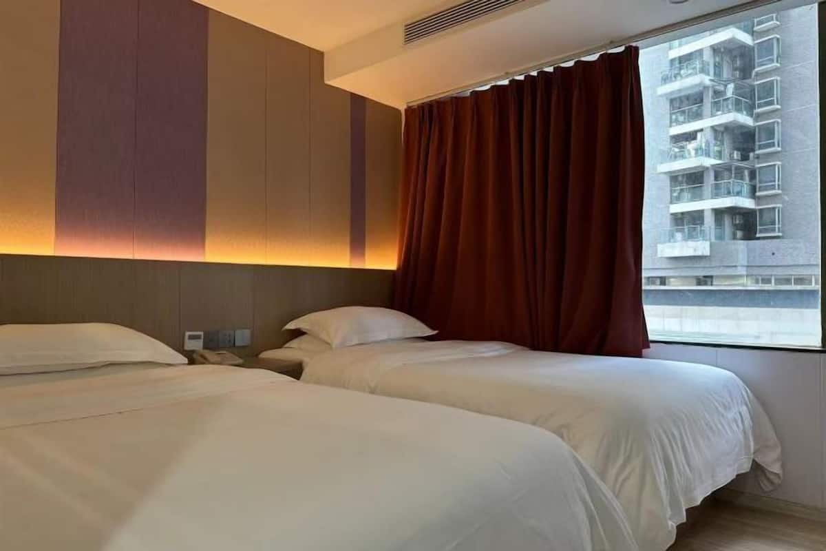 A hotel room with two beds, a window with curtains, and a view of a building.