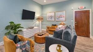 A living room with a flat-screen TV, two framed artworks, a wooden door, and a plant. - Brand New! Heart of Historic St. Augustine, Walk Everywhere, 4 Miles to Beach, Parking Spot, Balcony (St. Augustine)