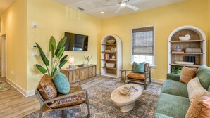 A spacious living room with a ceiling fan, a television mounted on the wall, and a bookshelf. - Brand New! Heart of Historic St. Augustine, Parking Spot, Balcony, Walk Everywhere, 4 Miles to Beach (St. Augustine)