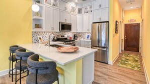 A modern kitchen with white cabinets, stainless steel appliances, and a central island with bar stools. - Brand New! Heart of Historic St. Augustine, Parking Spot, Balcony, Walk Everywhere, 4 Miles to Beach (St. Augustine)