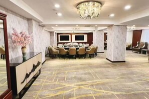 Un salón de conferencias con una mesa redonda, sillas, una araña y suelo alfombrado.