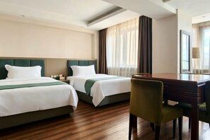 A hotel room with two beds, a desk, a chair, and a large window with curtains.