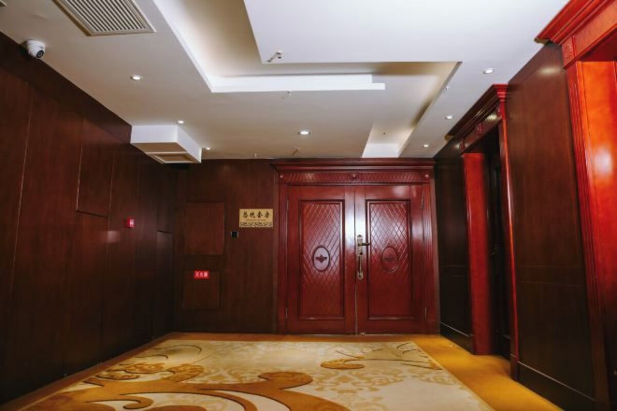 A hotel lobby with wooden paneling, a patterned carpet, and a double door with a sign above it.