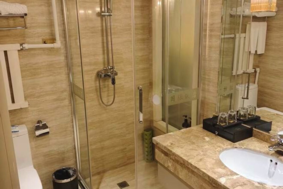 A bathroom with a glass-enclosed shower, a sink with a marble countertop, and a mirror.