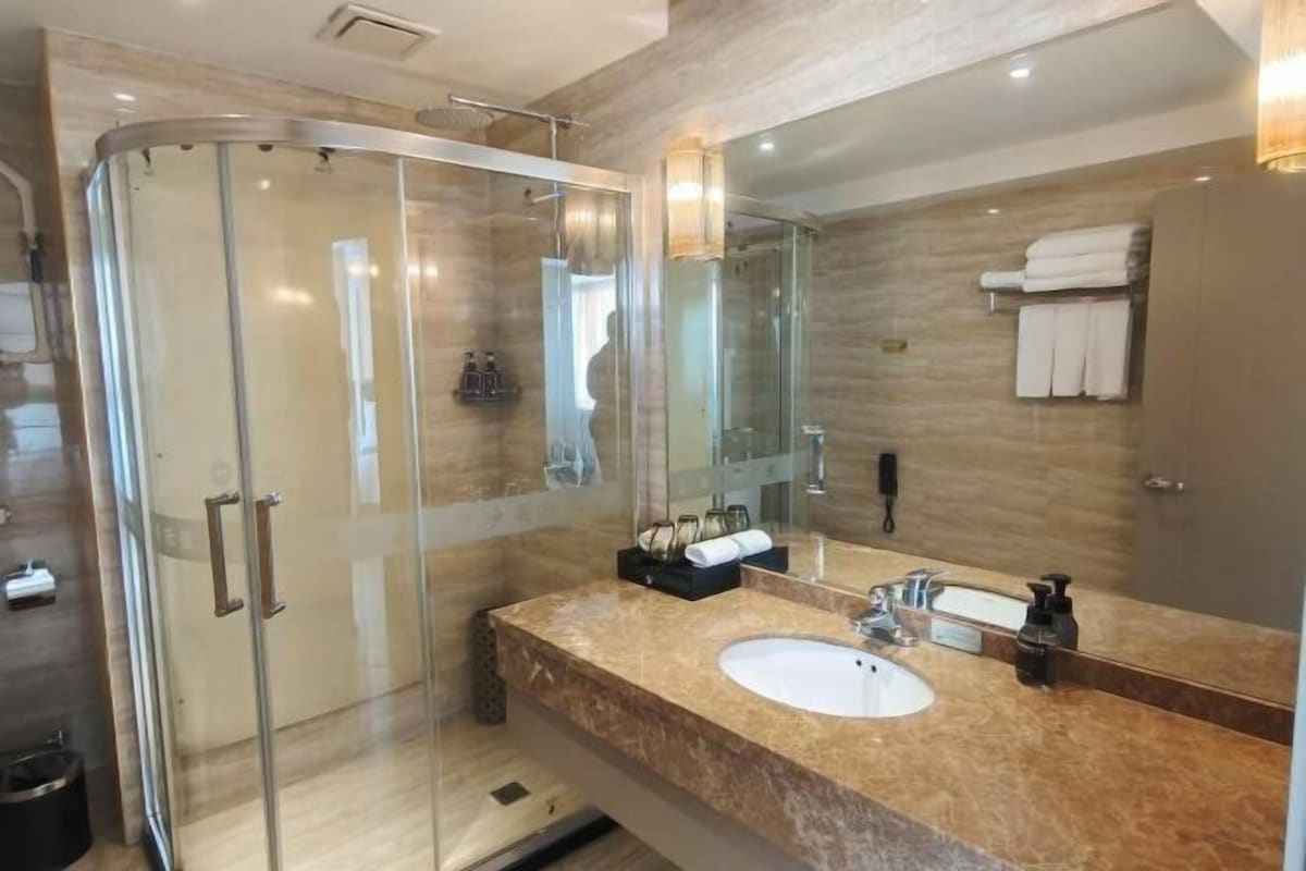 A modern bathroom with a glass-enclosed shower, a marble sink, and a large mirror.