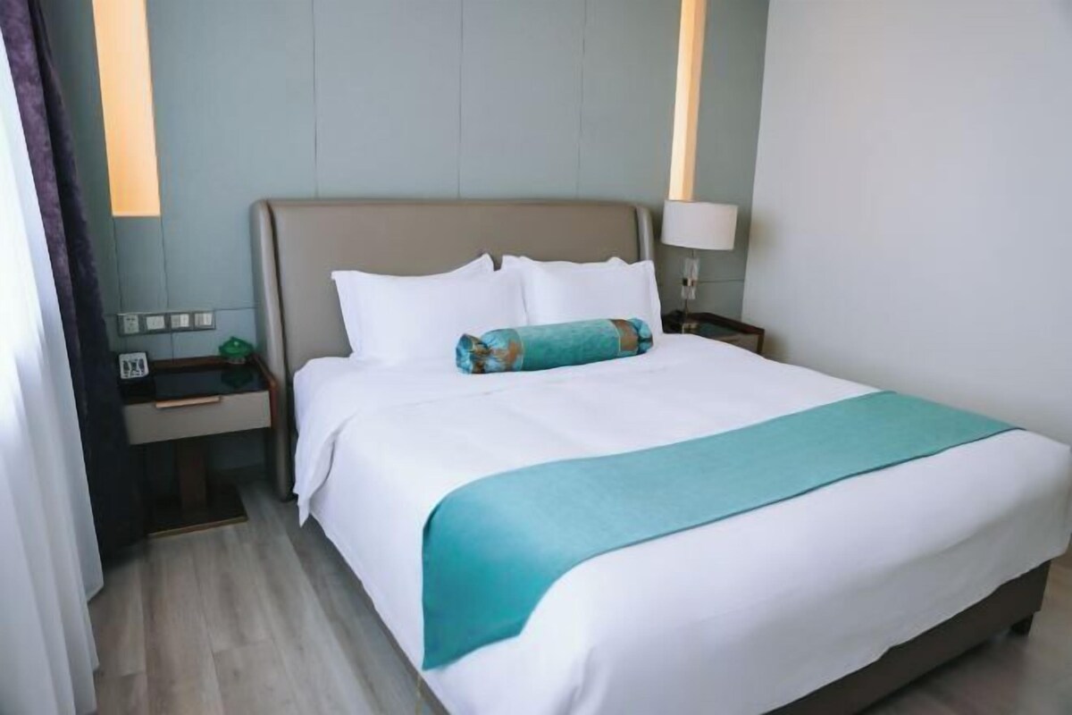 Een hotelkamer met een bed, nachtkastje, lamp en een wandlamp.