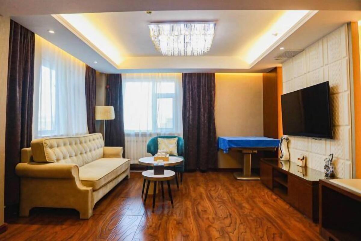 Hotellihuoneessa on sohva, pieni pyöreä pöytä, seinälle asennettu televisio ja puulattia.