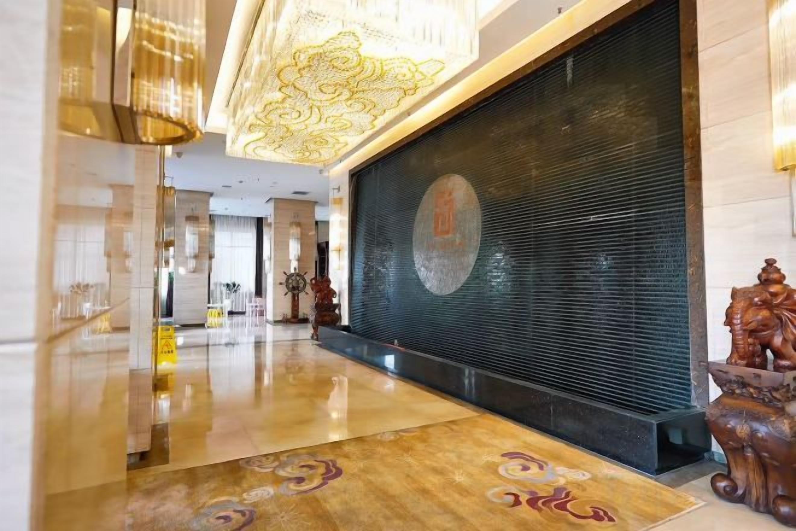 Un vestíbulo de hotel con piso pulido, un gran muro decorativo y una mesa de recepción.