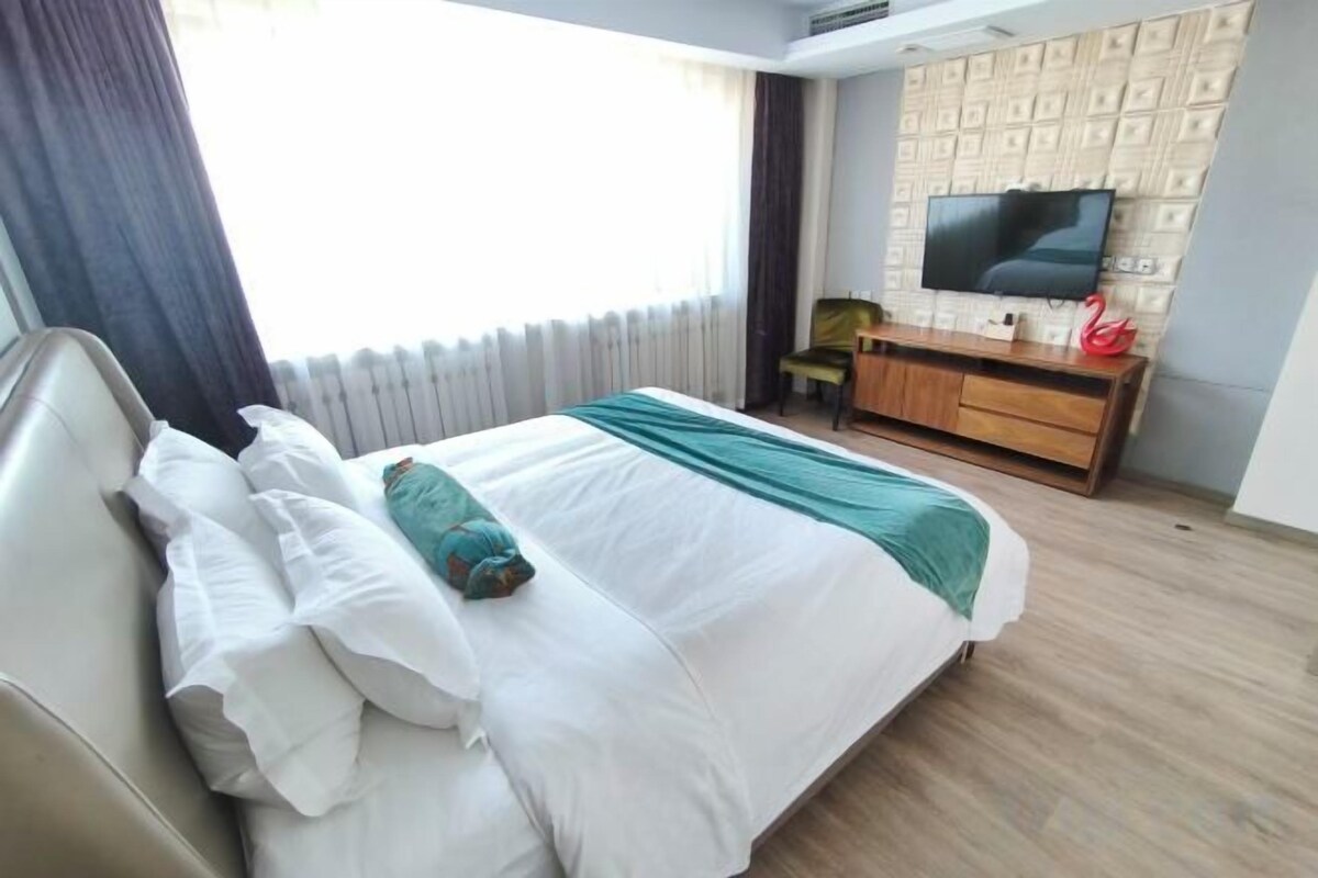 A hotel room with a bed, a television, a desk, and a window with curtains.