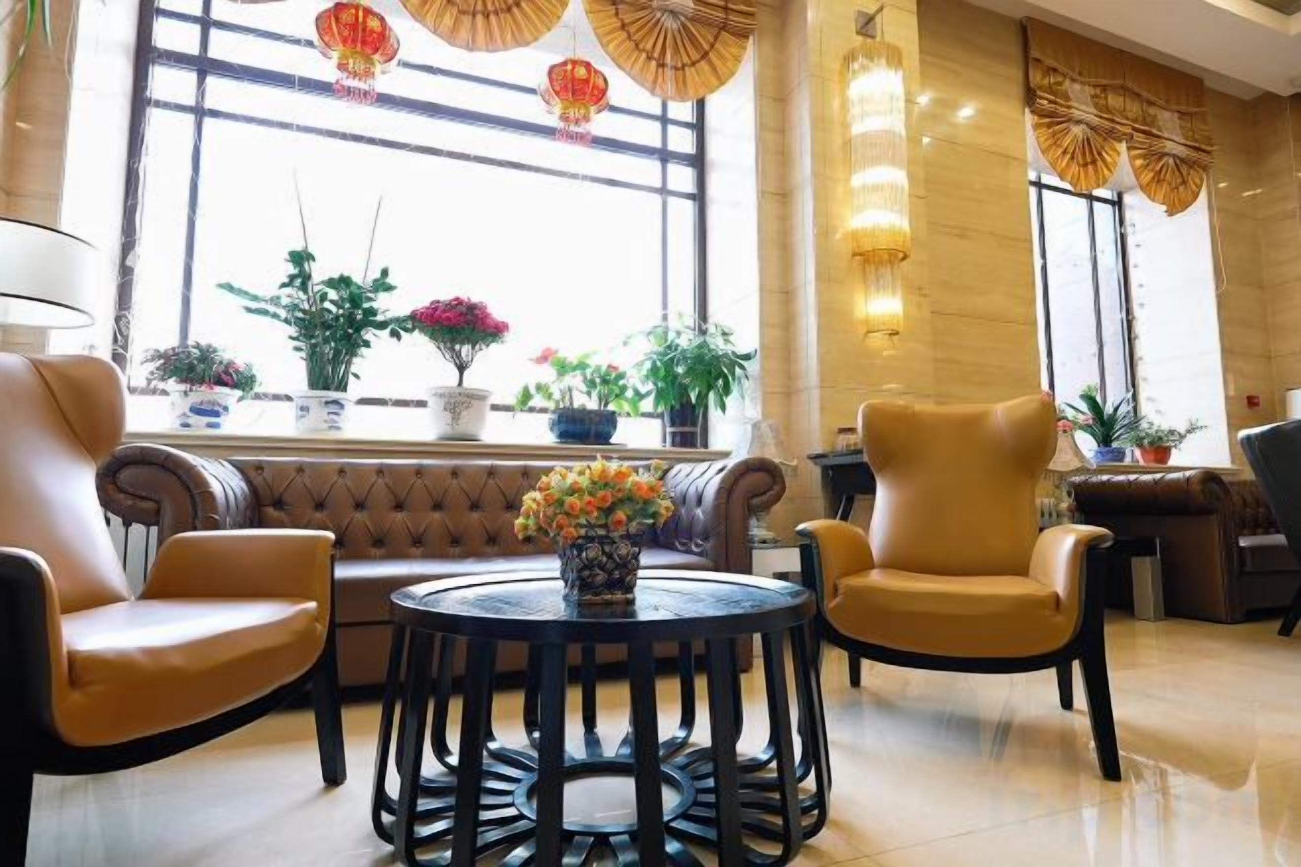 A lobby with leather sofas, a round table with a vase of flowers, and potted plants by the windows.