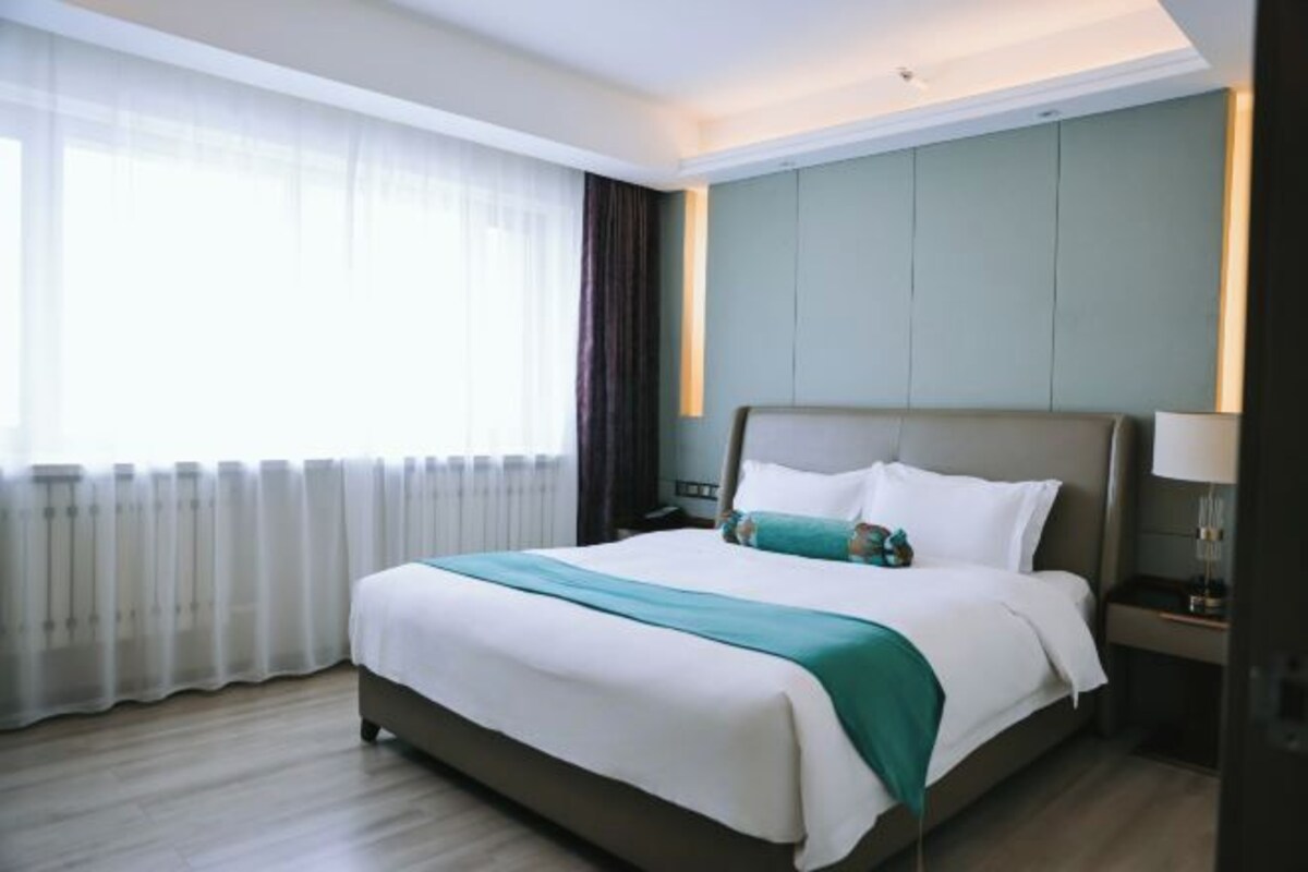 A hotel room with a large bed, a nightstand, a lamp, and a window with curtains.