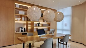 A modern meeting room with a wooden table, four chairs, a desktop computer, a laptop, and a bookshelf with books and decorative items. - Ji Hotel (Shanghai)