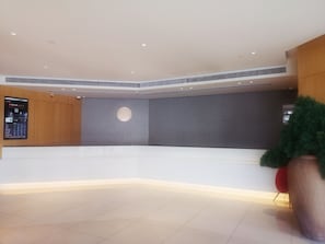 A spacious lobby with a modern design, featuring a large reception desk, a digital information board, and a potted plant. - Ji Hotel (Shanghai)