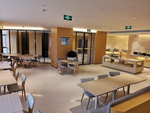 A modern dining area with tables and chairs, a kitchen counter, and exit signs on the ceiling. - Ji Hotel (Shanghai)