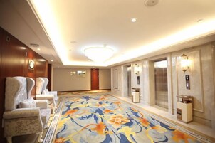 A hotel lobby with a carpeted floor, seating area, elevators, and wall-mounted lighting.